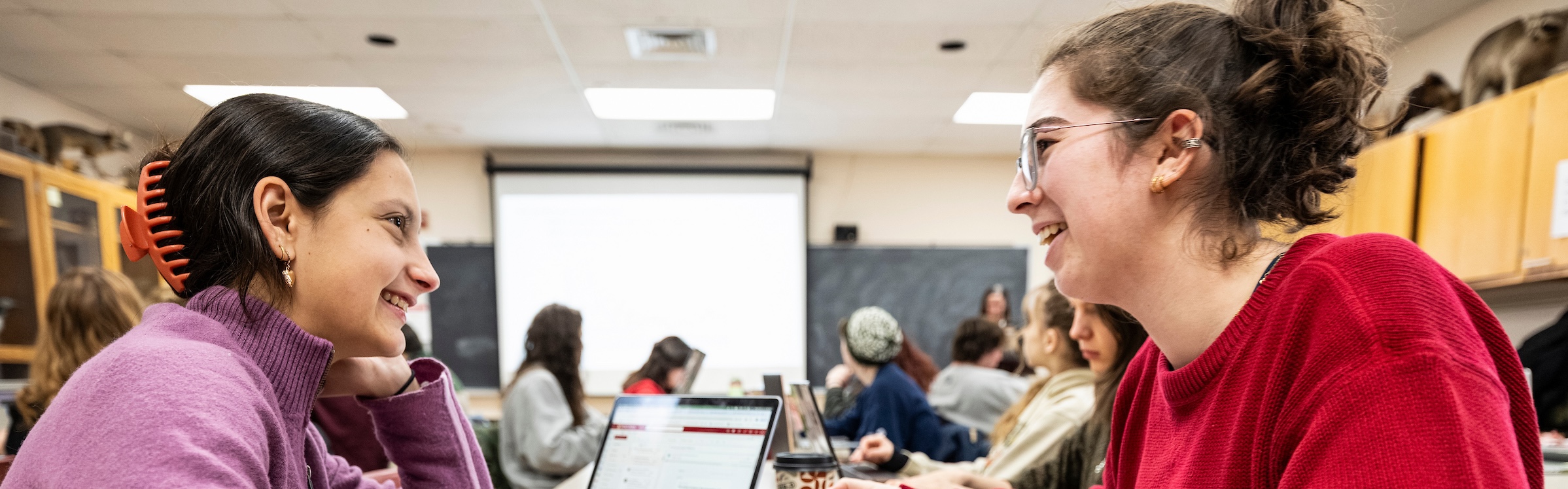 Photo of two students smiling and talking to one another during class.